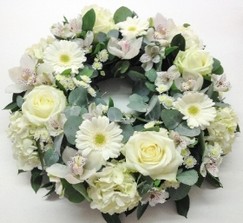 Classic funeral wreath with mixed white seasonal flowers, accented with complementary foliage.
