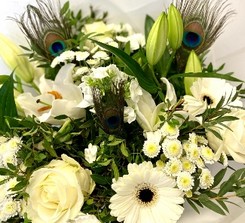 White seasonal florist’s choice hatbox arrangement with greenery and peacock feathers.