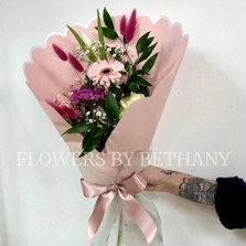 Hand-tied pink bouquet with seasonal florist’s choice florals and greenery, wrapped in scalloped blush pink paper with a satin ribbon.