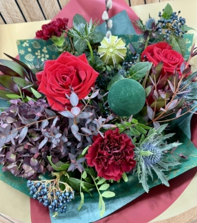 Luxury red Christmas bouquet with deep festive tones, winter textures and seasonal greenery arranged in a gift bag.