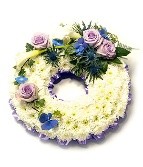 White chrysanthemum funeral wreath with a lilac and blue floral focal, accented with complementary flowers and mixed foliage.
